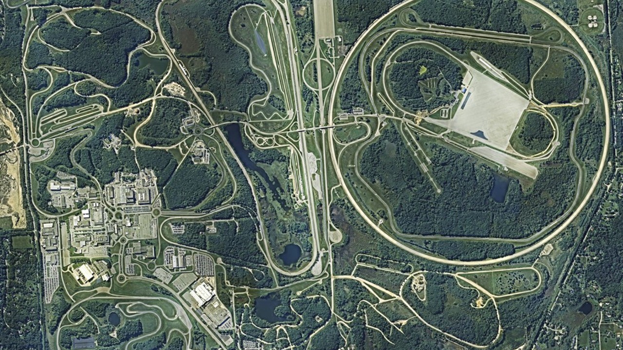 Aerial view of GM’s Milford Proving Ground, displaying high-speed test tracks and facilities in a forested landscape.
