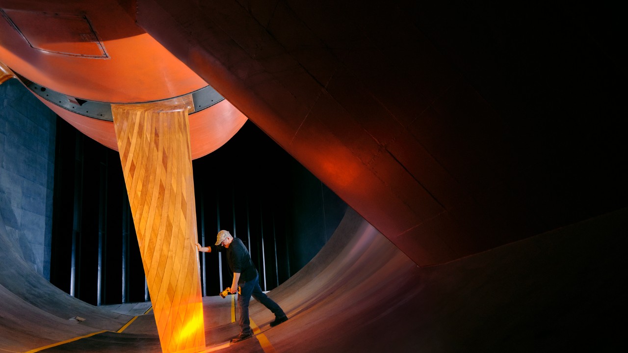 Engineer inspecting an orange vertical test panel inside a large automotive wind tunnel