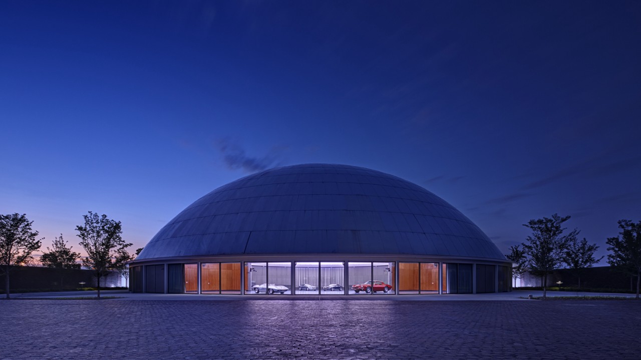 GM Design Dome illuminated at dusk showcasing historic concept vehicles through glass exterior